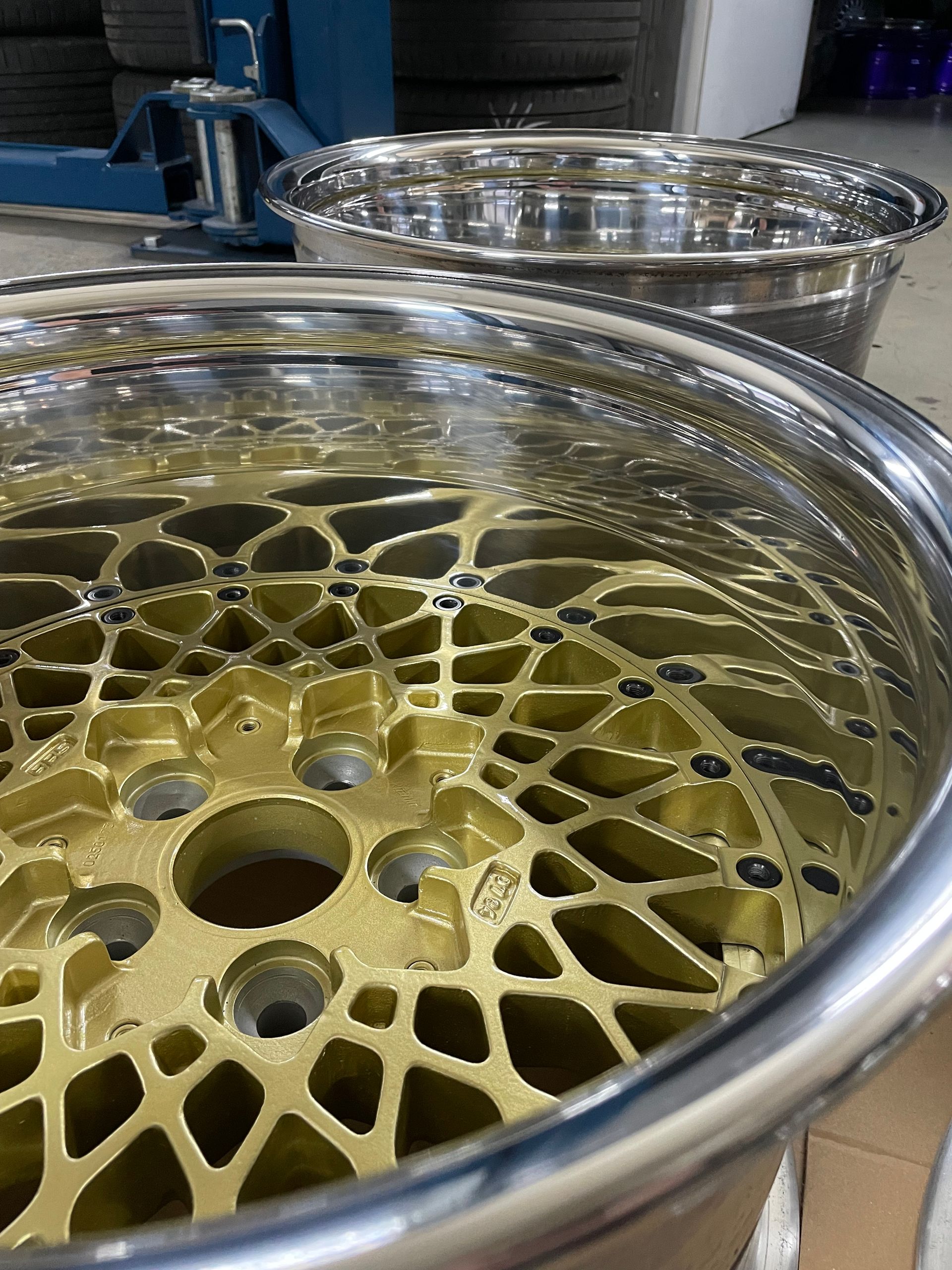 Zwei goldene und silberne Autofelgen mit einem komplexen netzartigen Muster, im Innenbereich.