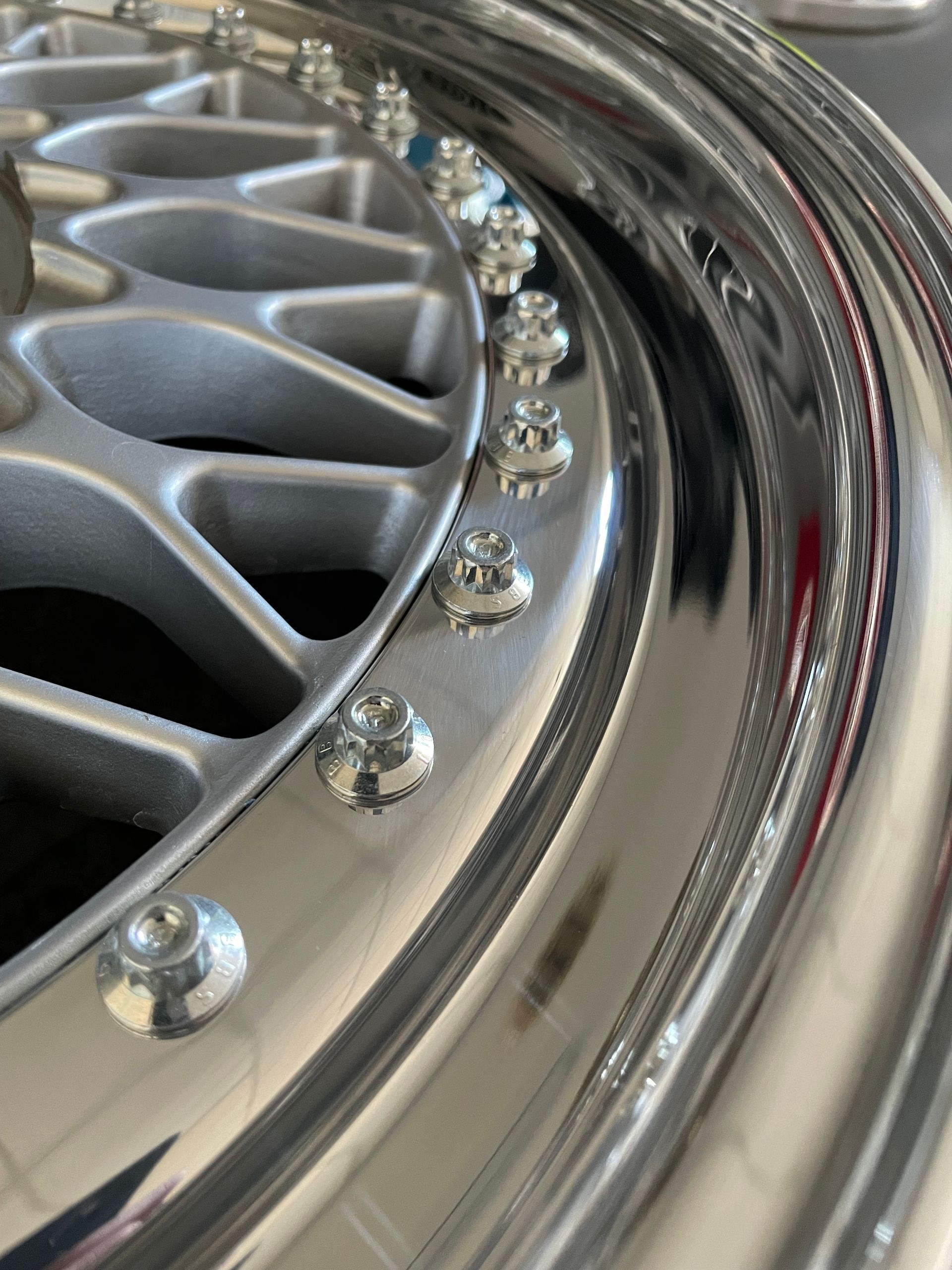 Nahaufnahme einer silbernen Autofelge mit poliertem, reflektierendem Außenrand und silbernen Schrauben.