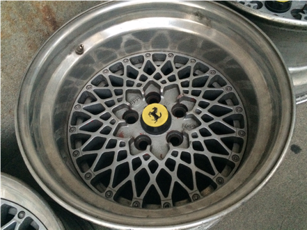 Silber-graue Leichtmetallfelge mit spinnennetzartigem Design und gelbem Ferrari-Emblem in der Mitte.
