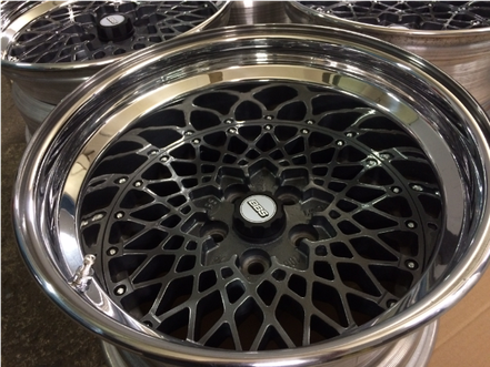 Nahaufnahme von vier Autorädern mit verchromtem Außenrand und einem komplexen, netzartigen schwarzen Zentrum.