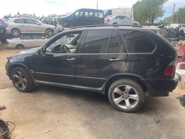 Un SUV negro estacionado en un terreno de tierra con otros vehículos al fondo.