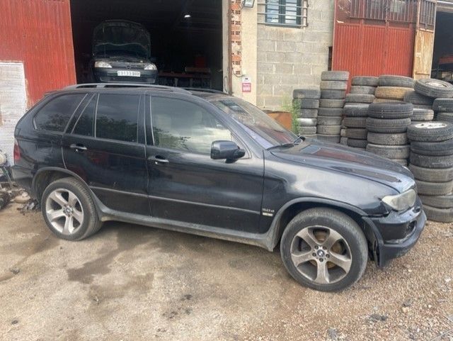 Un SUV negro estacionado junto a un garaje con neumáticos apilados y un edificio rojo.