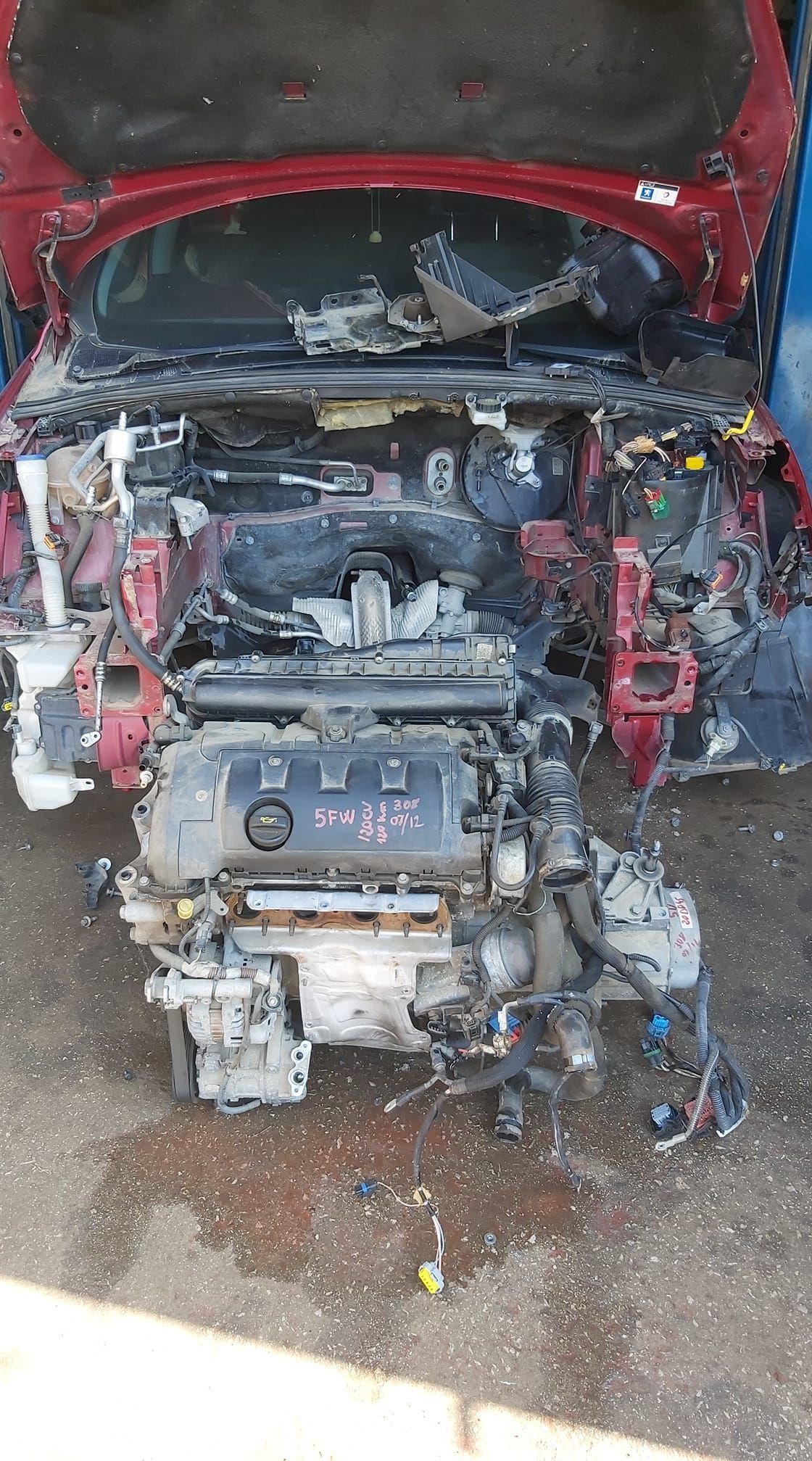 Parte delantera de un coche rojo quemado con el motor al descubierto y el capó abierto.