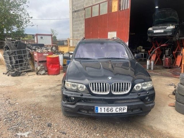 SUV BMW negro estacionado afuera de un taller mecánico con bahía abierta y neumáticos cerca.