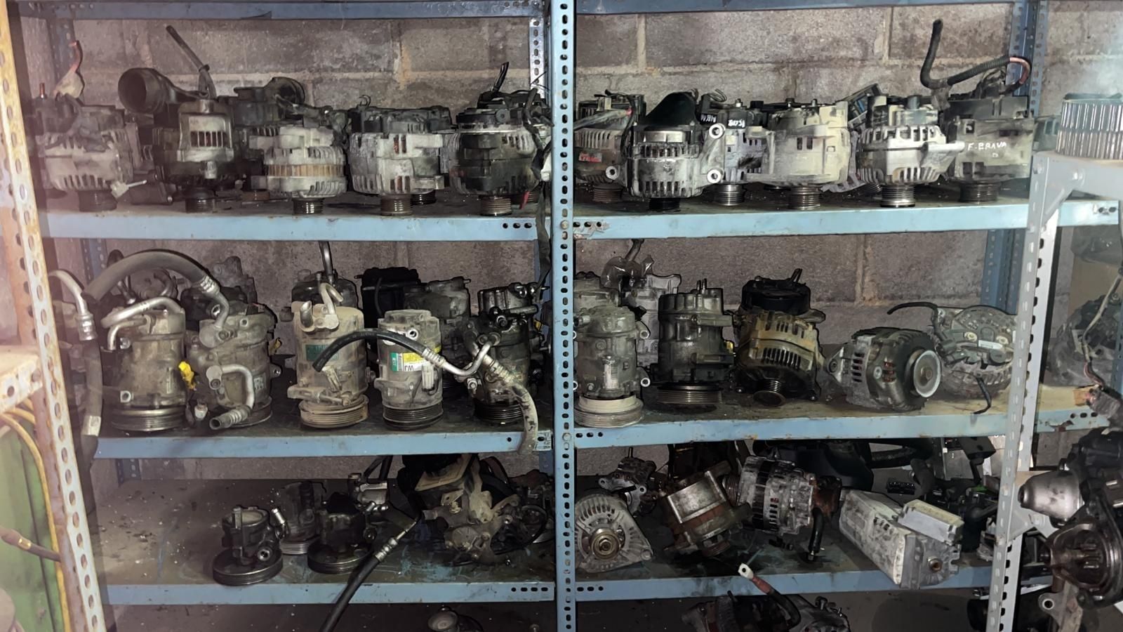 Estanterías en un taller polvoriento repletas de viejas piezas mecánicas, motores y herramientas de metal.