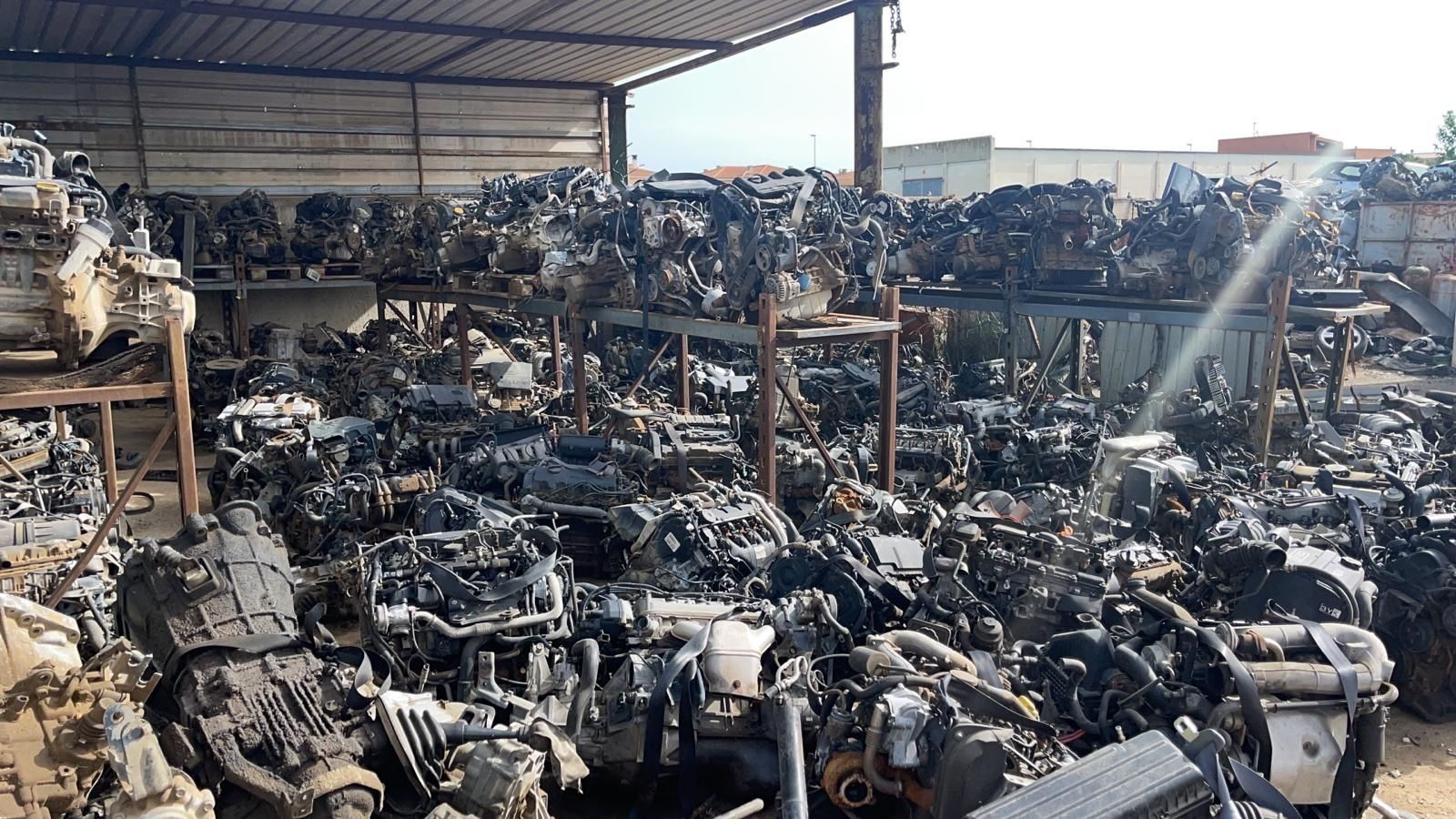 Piezas de motocicleta y motor gravemente quemadas apiladas en un desguace bajo un techo de metal.