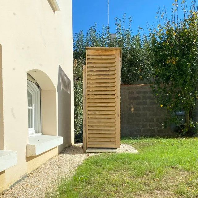 Chauffage PAC dont le groupe extérieur dans le jardin est caché par une structure en bois