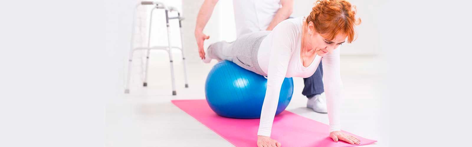 Una mujer está sentada en una colchoneta de yoga con una pelota de ejercicio azul.