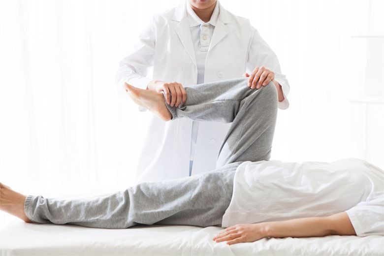 Un médico está estirando la pierna de un paciente en una cama.