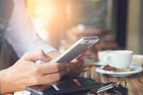 Personne utilisant un smartphone, cadre de café ensoleillé avec café et clés sur la table.