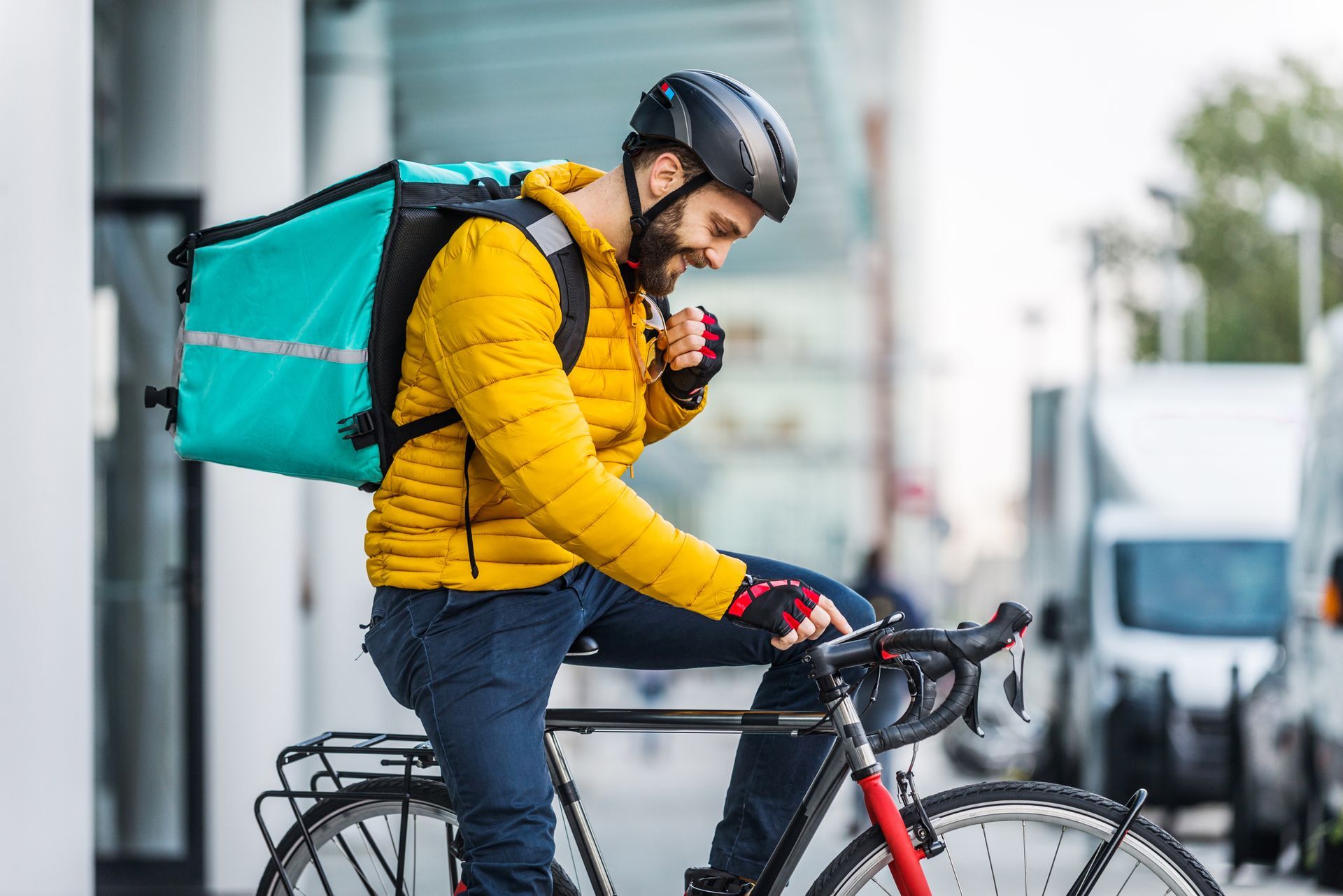 Homme en veste jaune sur vélo avec sac de livraison, souriant à l'extérieur.