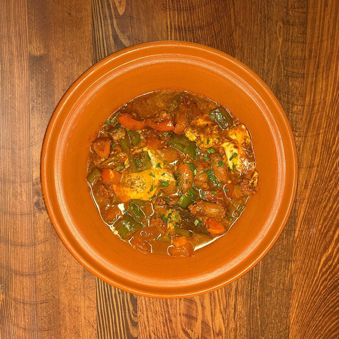 Tajine tunisien aux légumes dans un bol en terre cuite sur une table en bois.