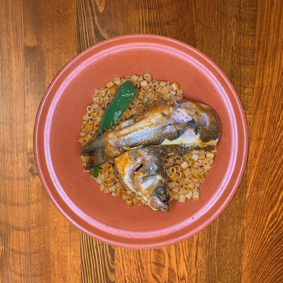 Plat de poisson avec des pâtes et un poivron vert dans un bol en terre cuite sur une table en bois.