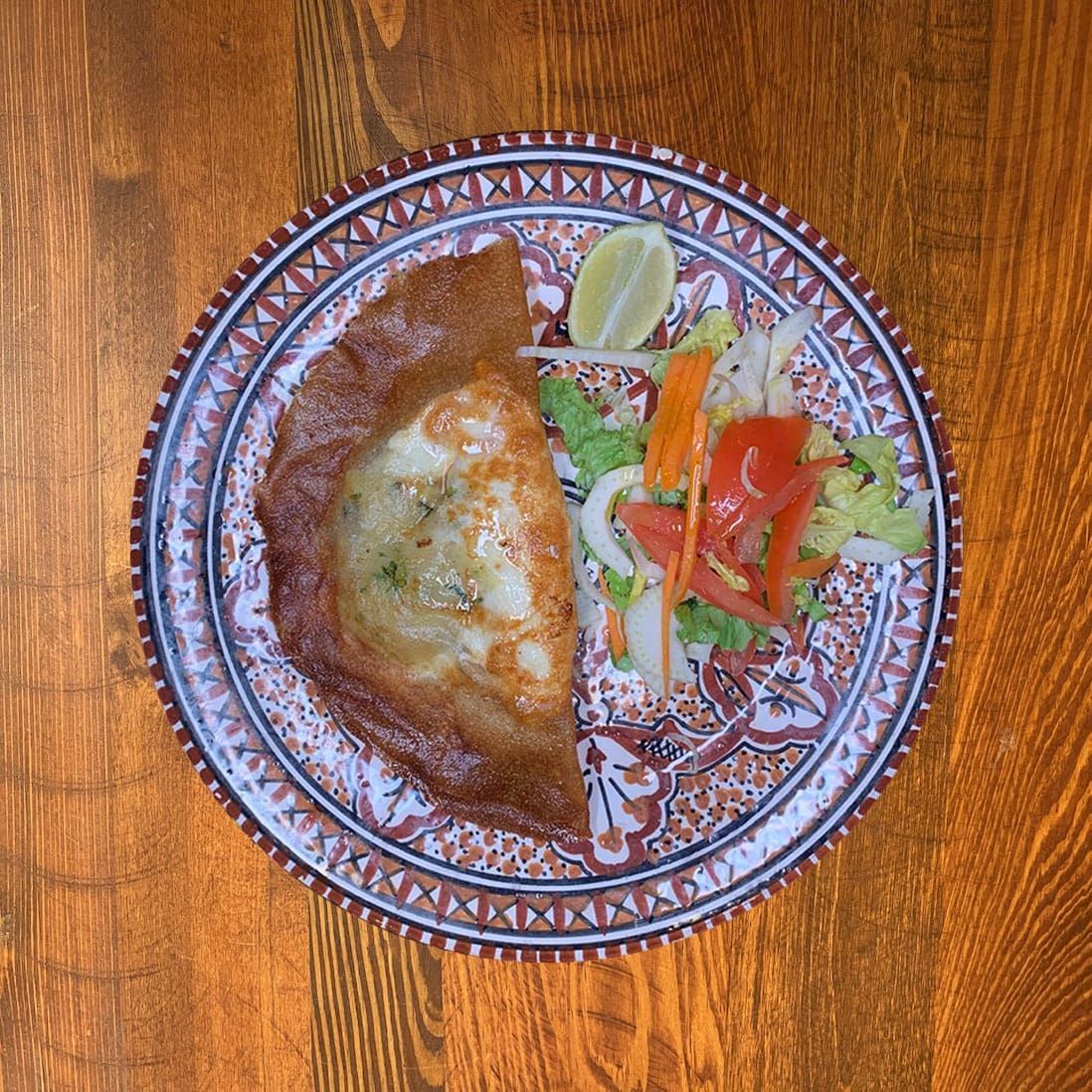 Une assiette de nourriture avec une pâte fourrée cuite au four, une salade et un quartier de citron.