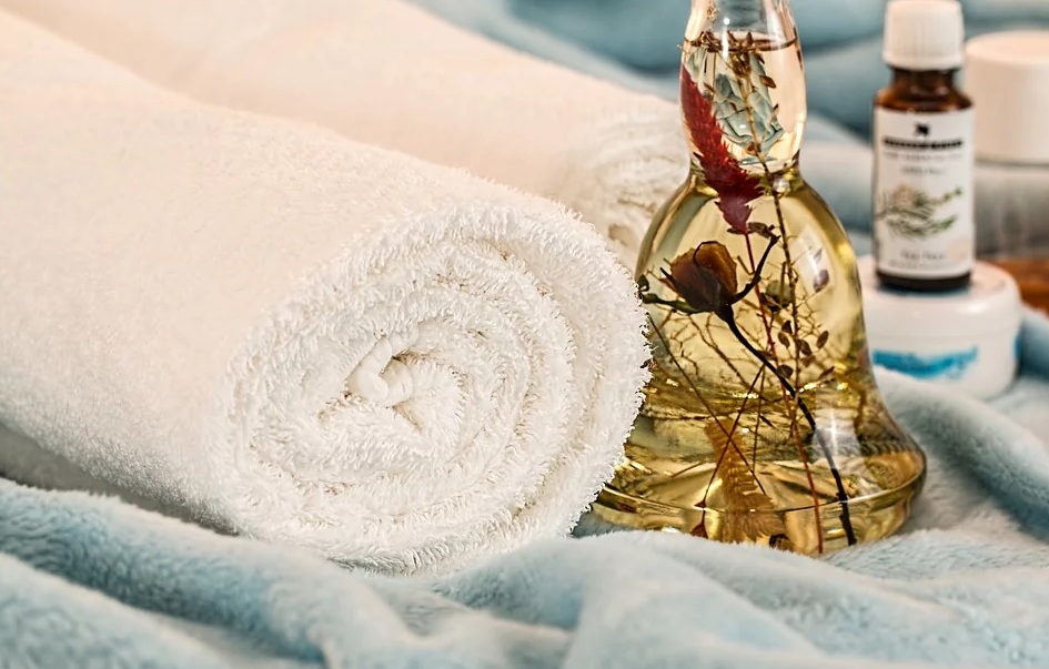 Photo d'une serviette enroulée sur elle-même avec un flacon d'huile de massage à côté