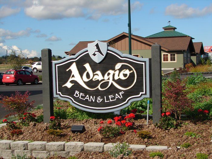 Sign for Adagio Bean & Leaf cafe with dark posts, brown building background.