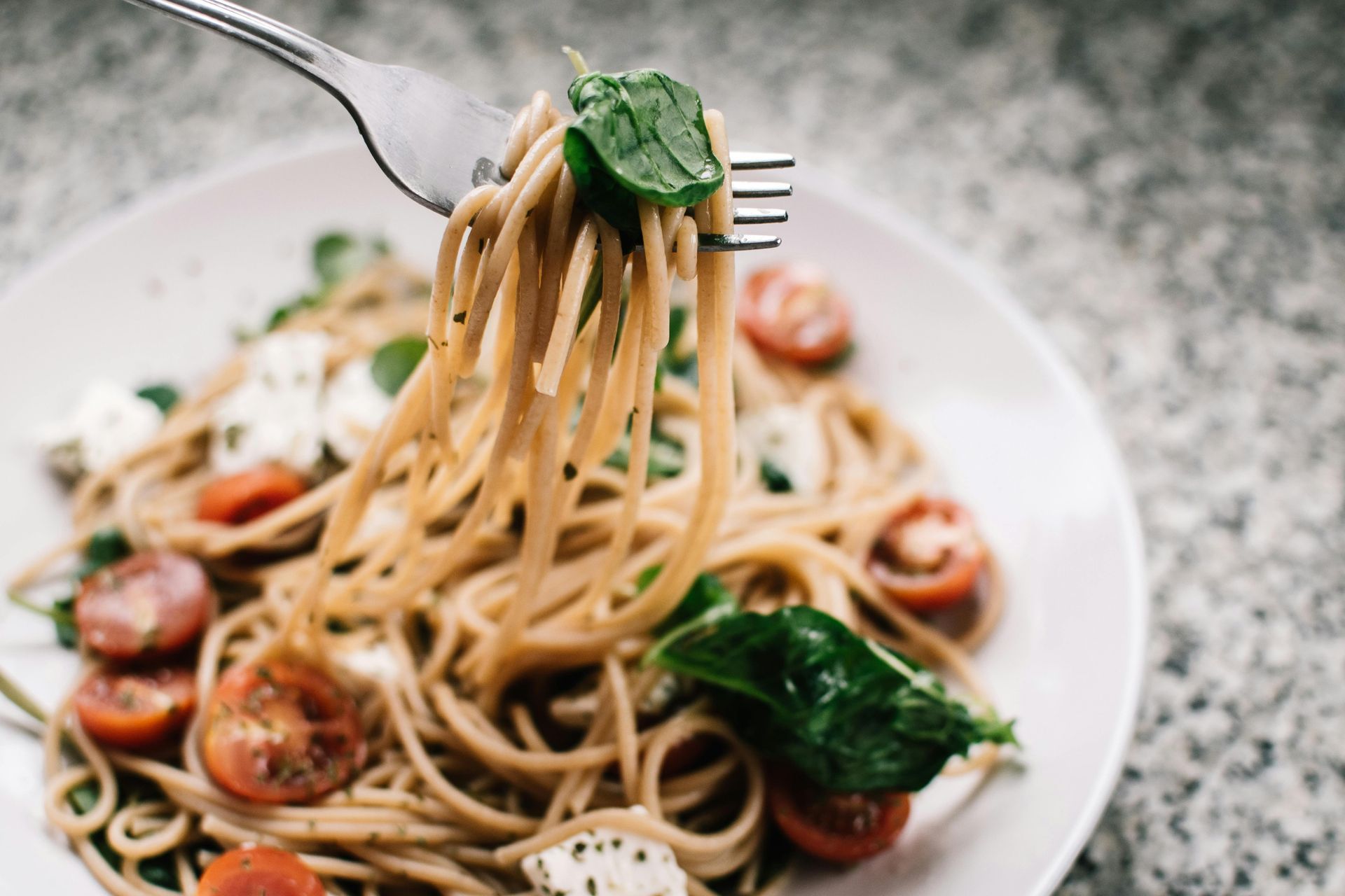 Pasta dish: spaghetti, tomatoes, basil, and mozzarella on a plate, being lifted by a fork.