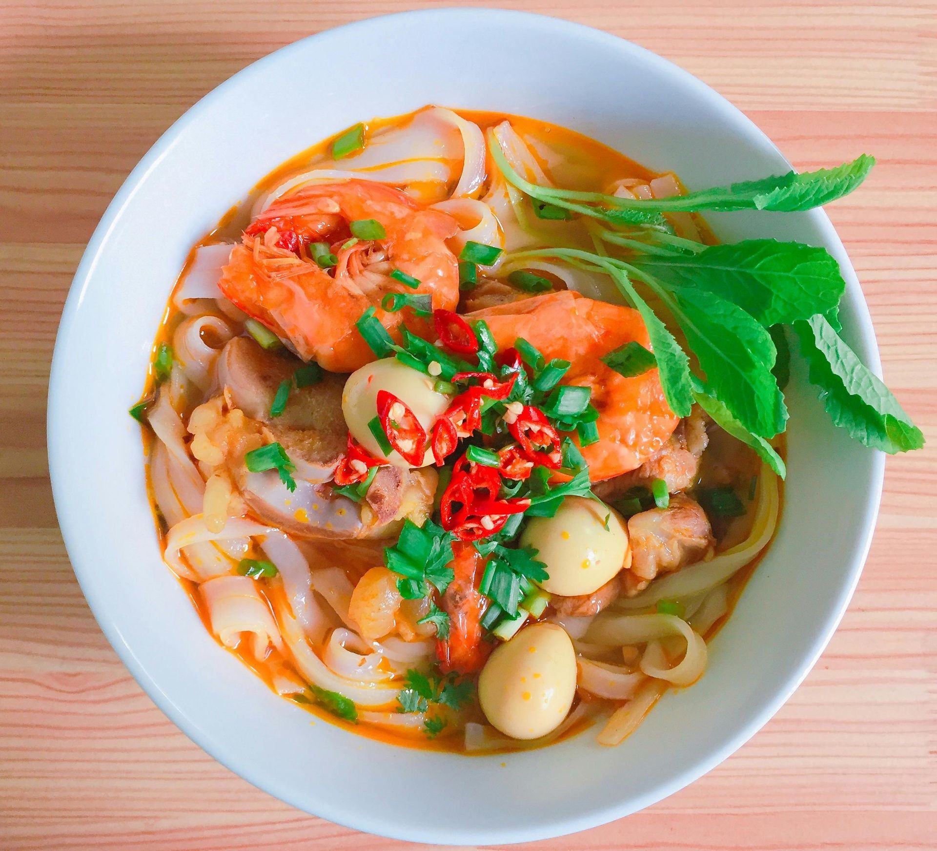 Bowl of Vietnamese noodle soup with shrimp, quail eggs, and herbs.