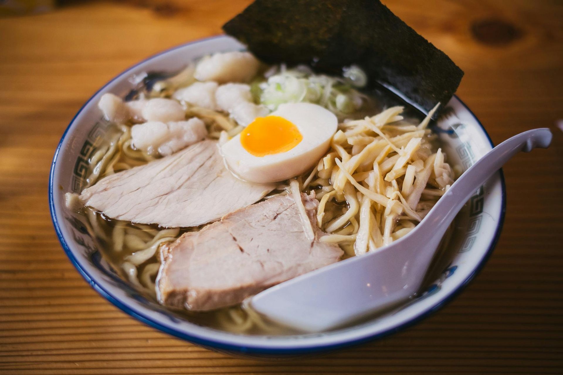 Ramen bowl with noodles, pork slices, egg, seaweed, and scallions; wooden table.