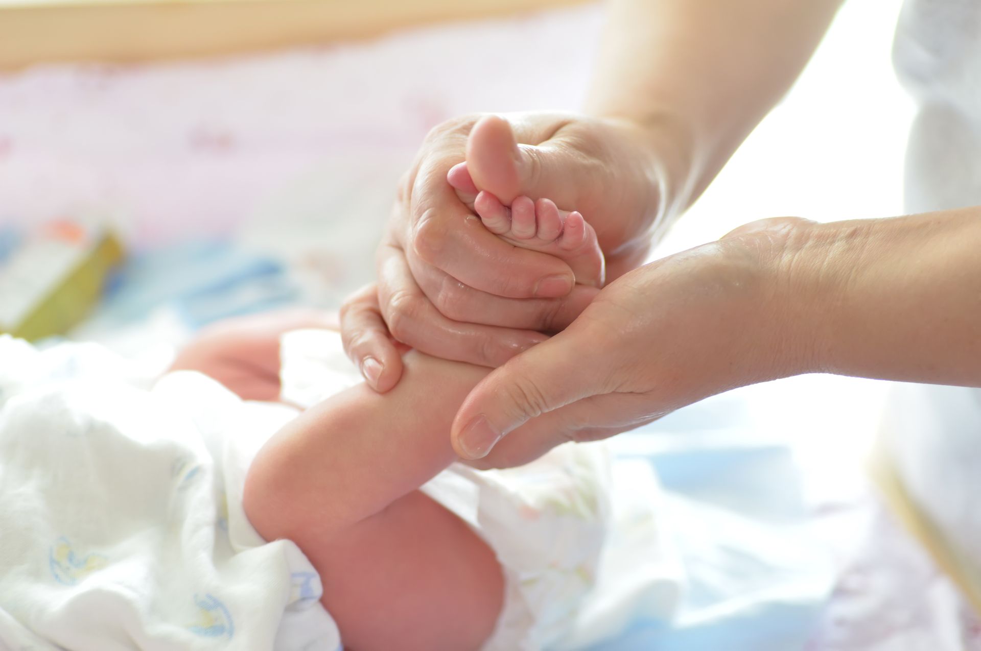 Mãos massageando delicadamente o pezinho de um bebê deitado sobre um tecido branco.