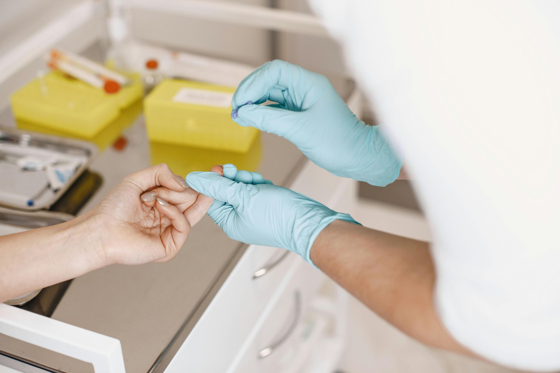Um profissional de saúde usando luvas azuis realiza um exame de sangue por punção digital em um paciente.