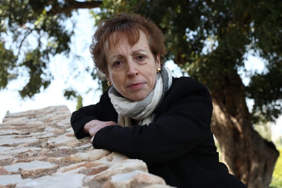 Una mujer apoyada en un muro de piedra con un árbol al fondo.