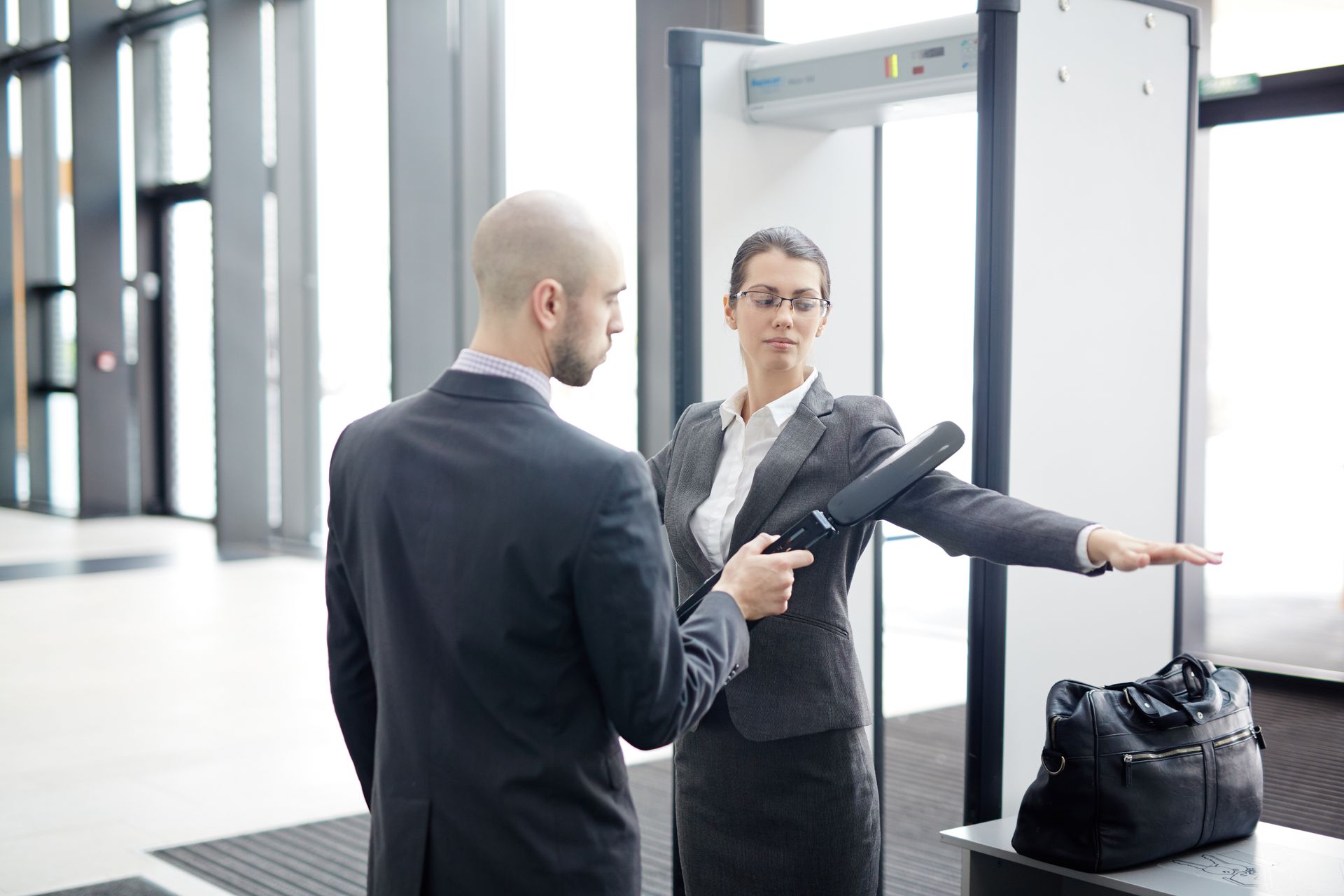 Un homme est scanné par un agent de sécurité avec un détecteur portatif à un portique de détection de métaux.