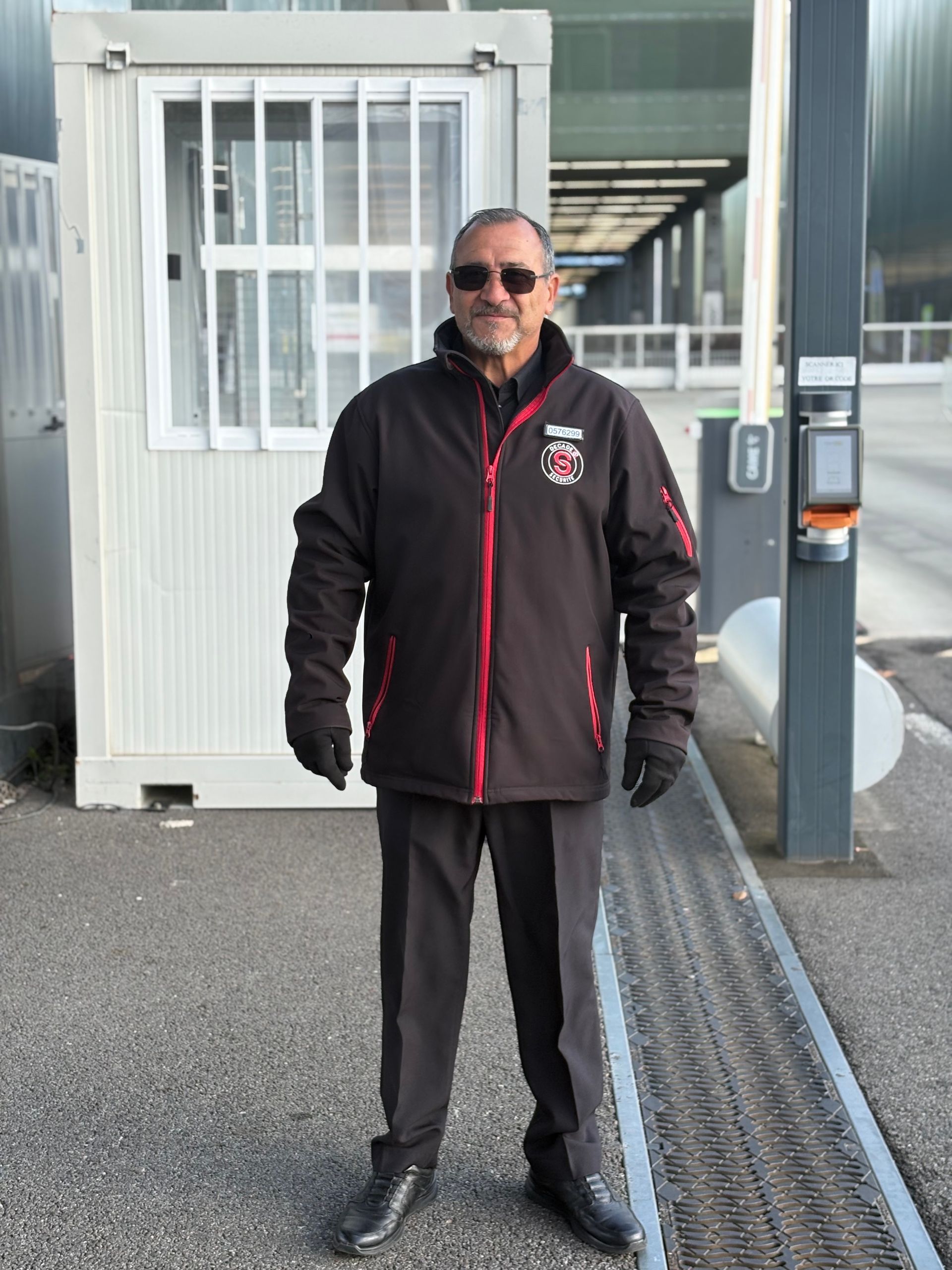 Un homme en costume tenant une corde en velours rouge lors d'un événement, gardant l'entrée.