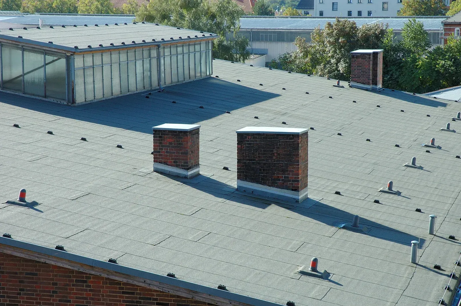Flat gravel rooftop with two brick chimneys and a small glass-roofed structure in the background