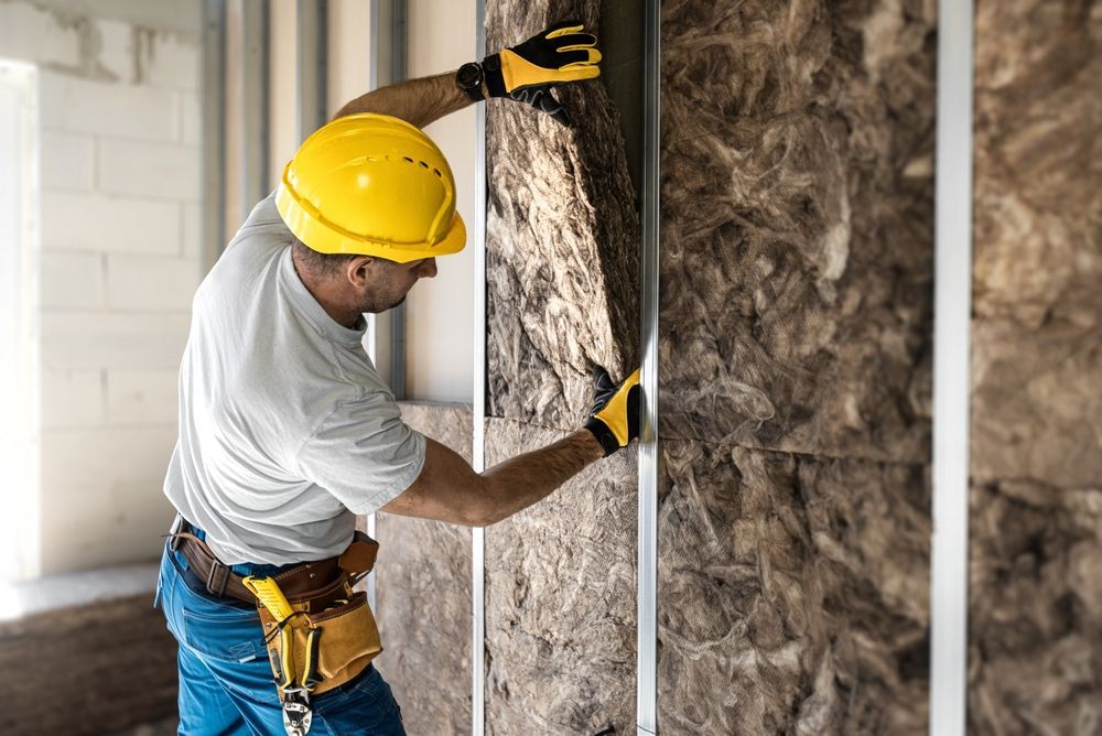 Obrero de la construcción instalando aislamiento en una pared, usando guantes y casco.
