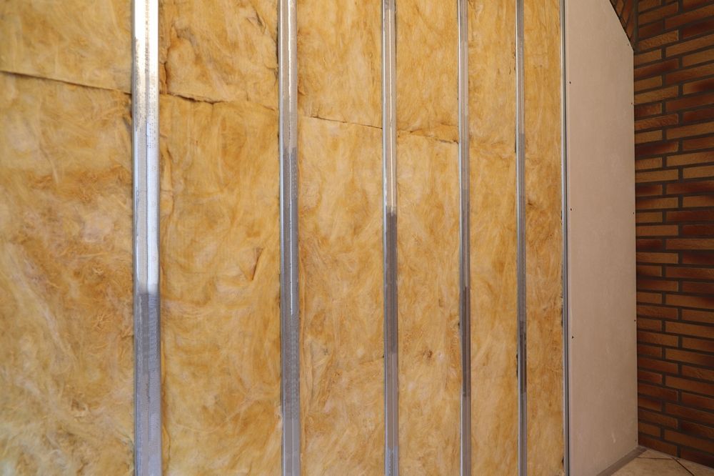 Pared interior en construcción que muestra aislamiento entre montantes metálicos, cerca de la pared de ladrillo.