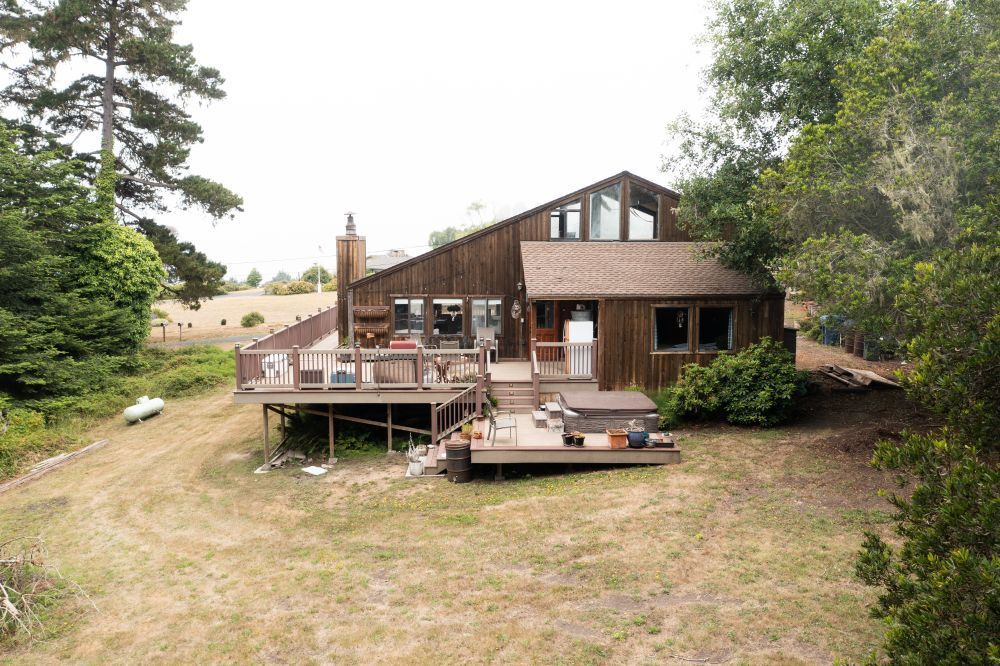 Brown wooden house with a deck, surrounded by trees and dry grass.