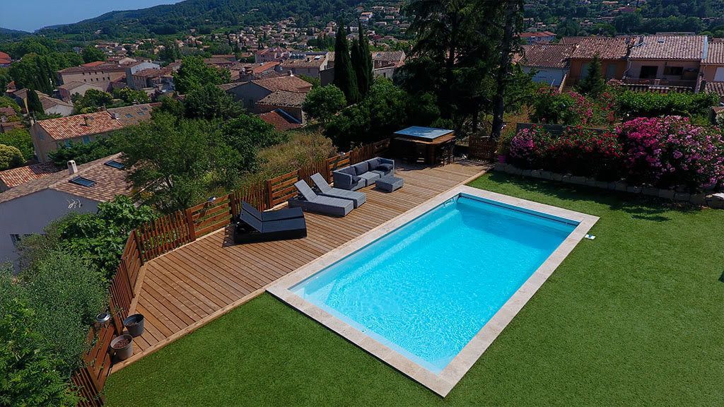 Une piscine dans un jardin avec une terrasse en bis et des transats