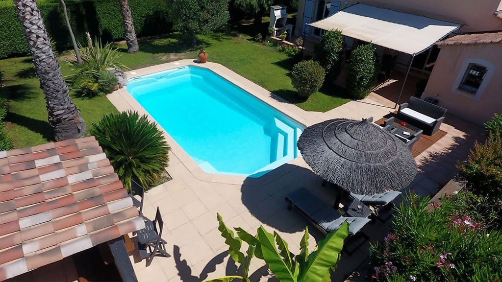 Une piscine avec des arbres, une maison et un parasol