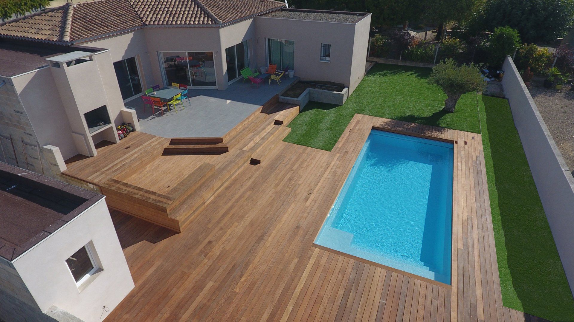 Une piscine avec une maison, une terrasse en bois et un jardin 