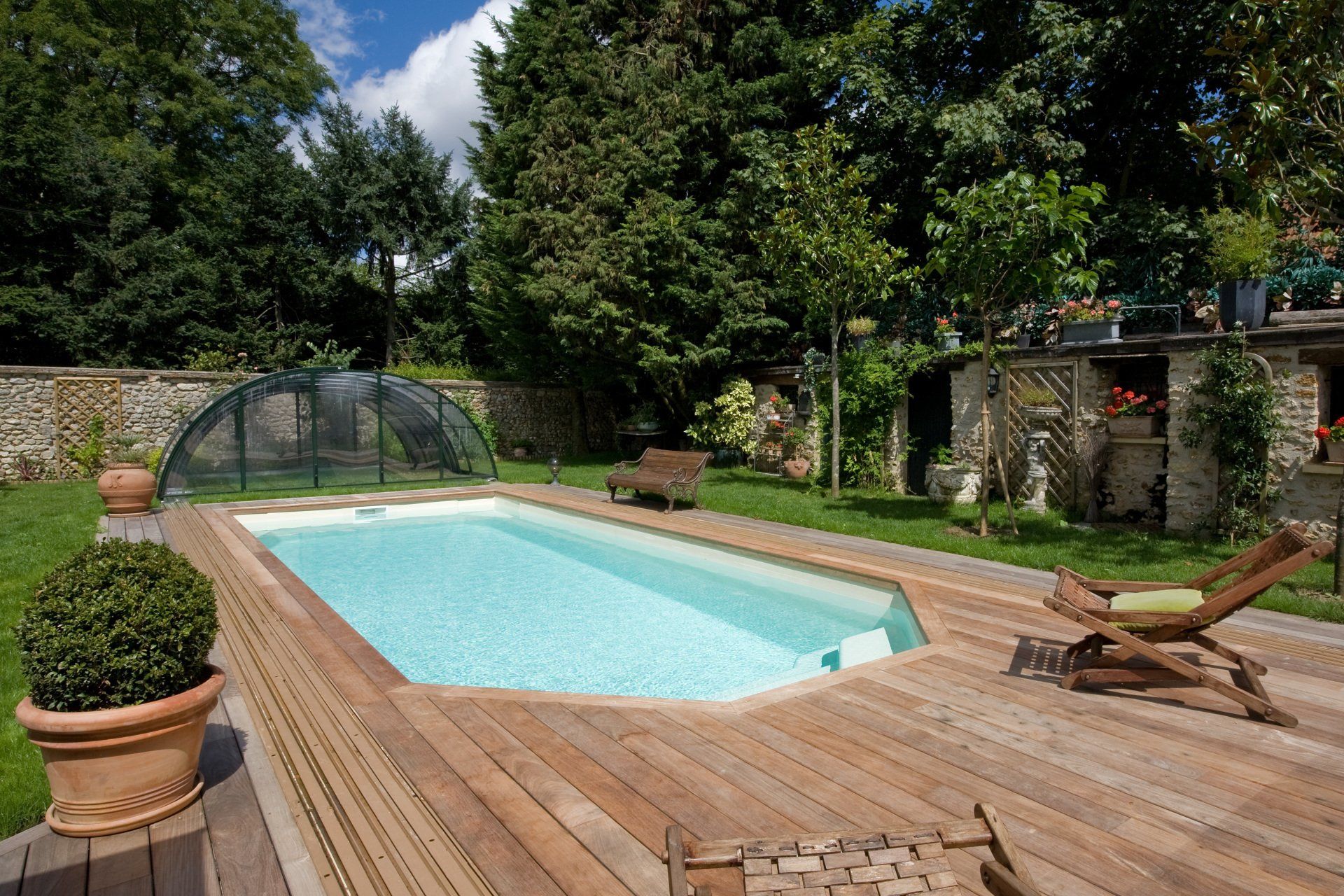 Une piscine avec une terrasse en bois, des transats en bois et de la verdure
