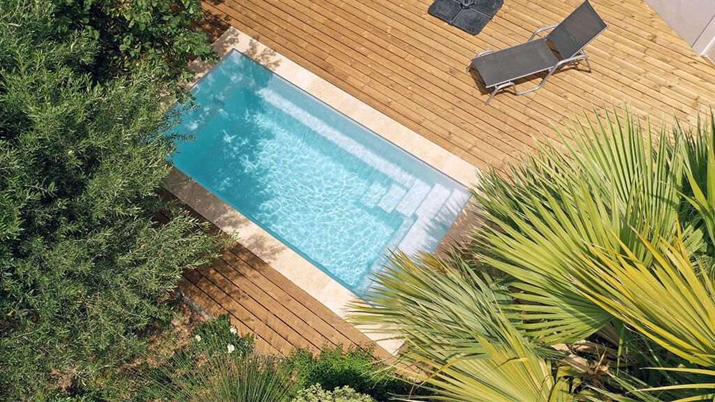 Une mini piscine avec une terrasse en bois, des arbustes et des transats