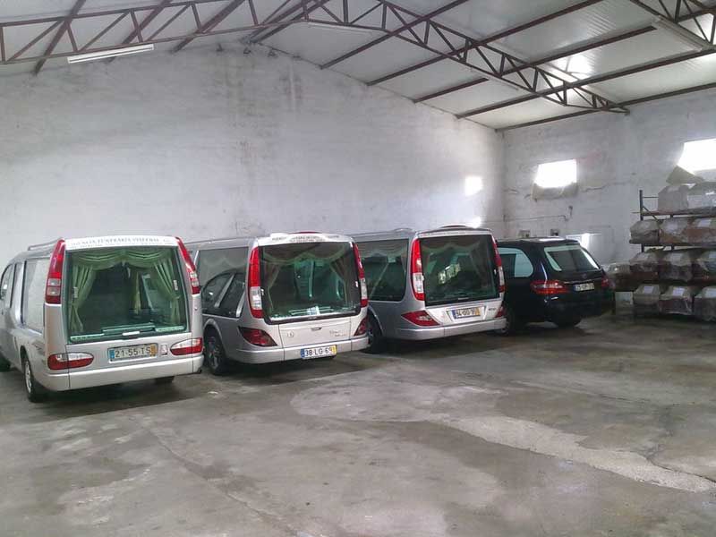 Carros funerários estacionados dentro de um grande armazém aberto.