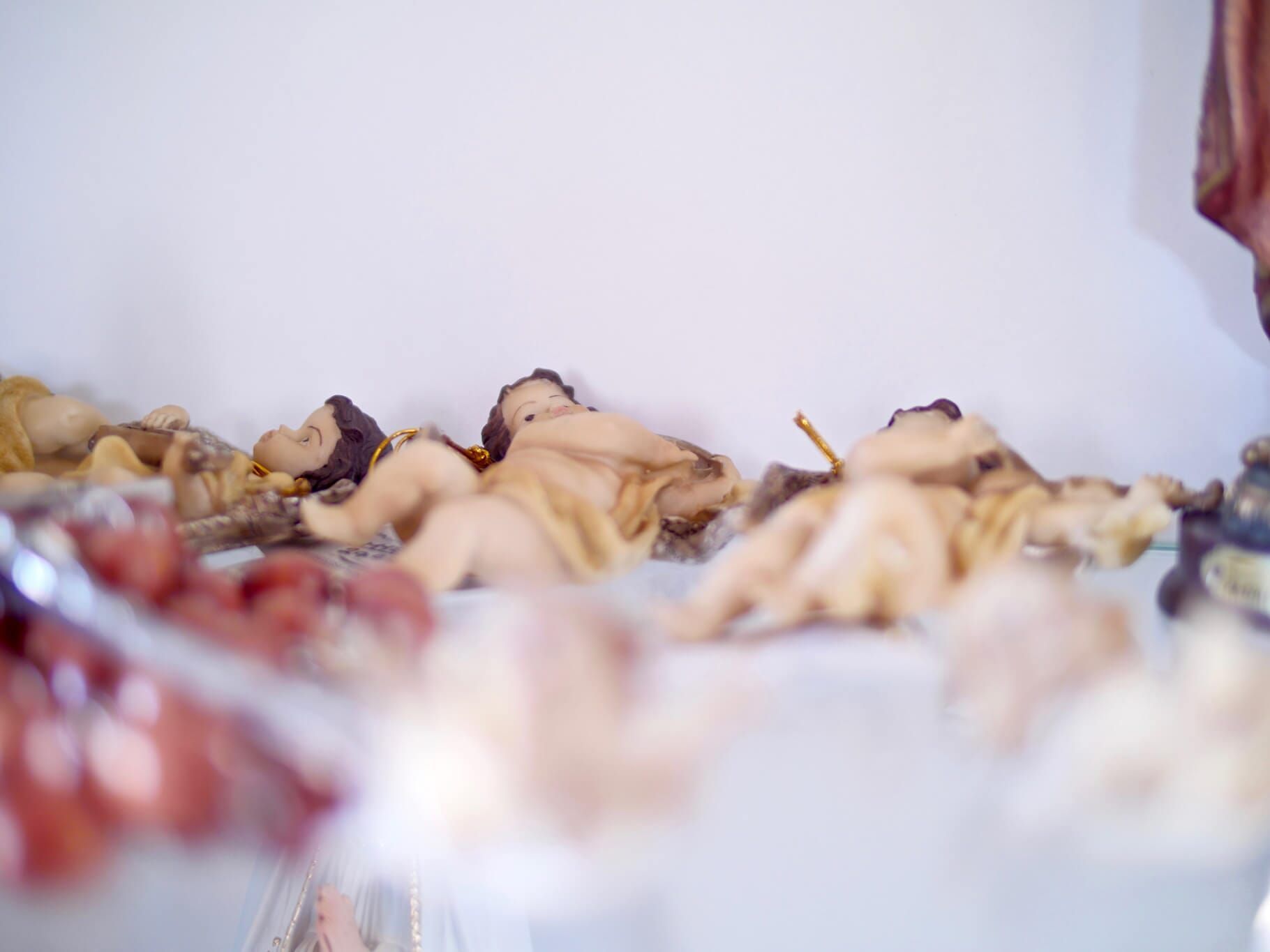 Prateleira com várias pequenas figuras de querubins reclinados. Tons de bege e bege, fundo branco.