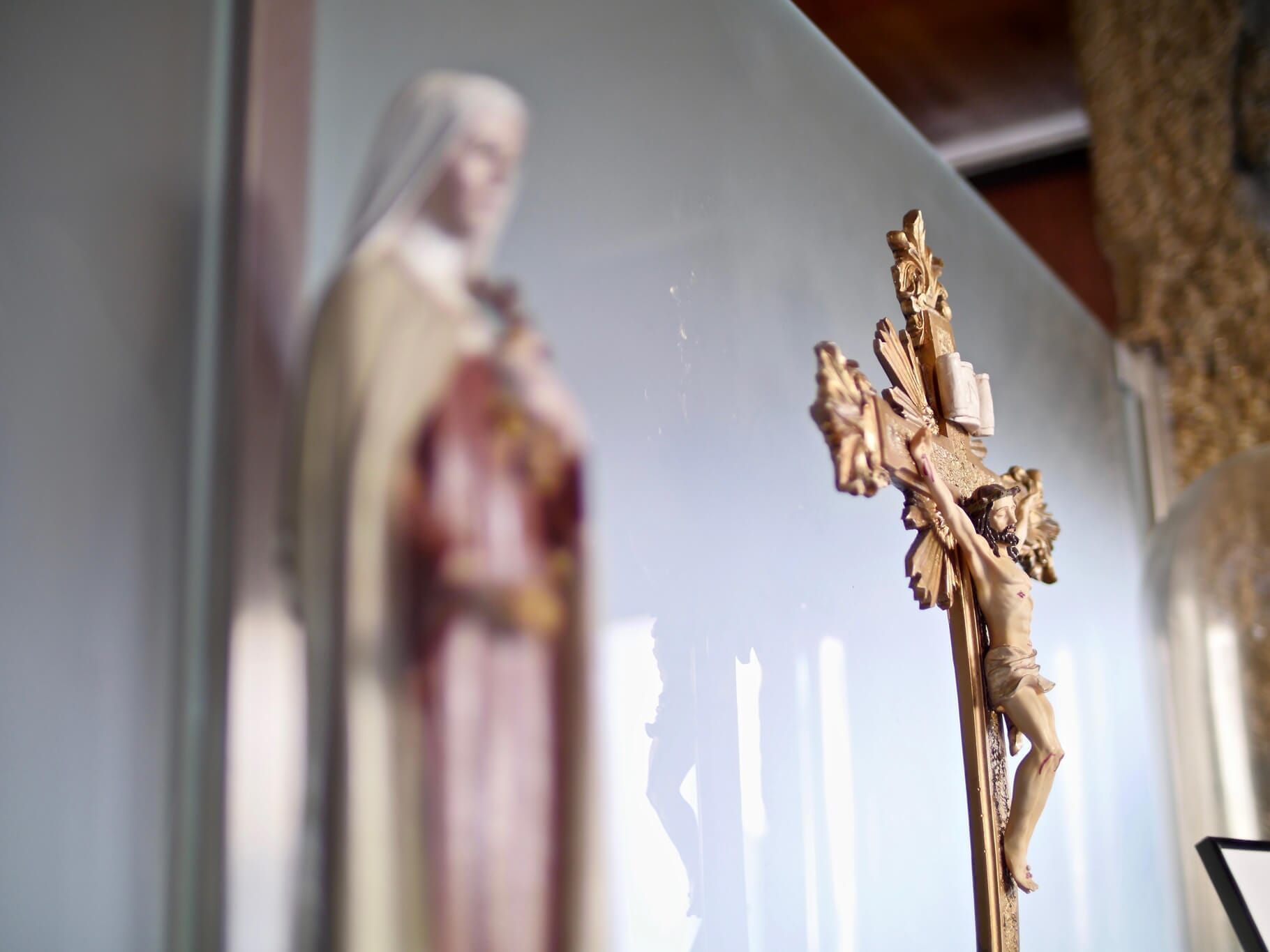 Estátua da crucificação em foco, com uma estátua desfocada de uma figura vestida com uma túnica ao fundo.