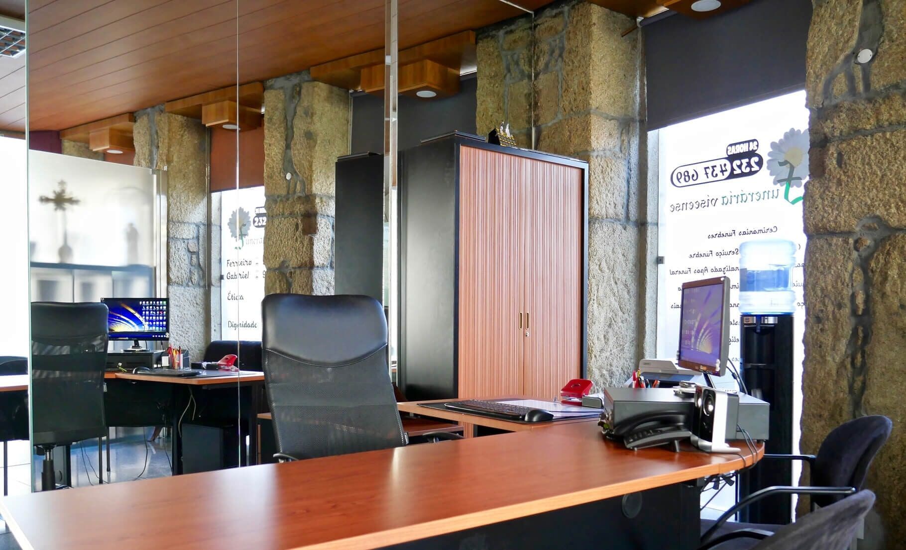 Interior de escritório com mesas, cadeiras, armário de armazenamento, computadores e colunas de pedra decorativas.