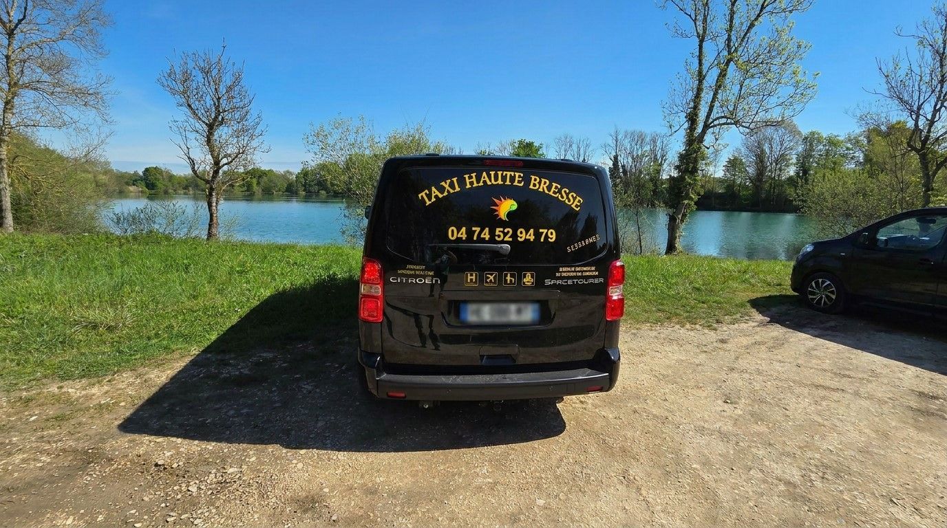 Un minibus noir garé au bord d'un lac, vue de l'arrière, par une journée ensoleillée.