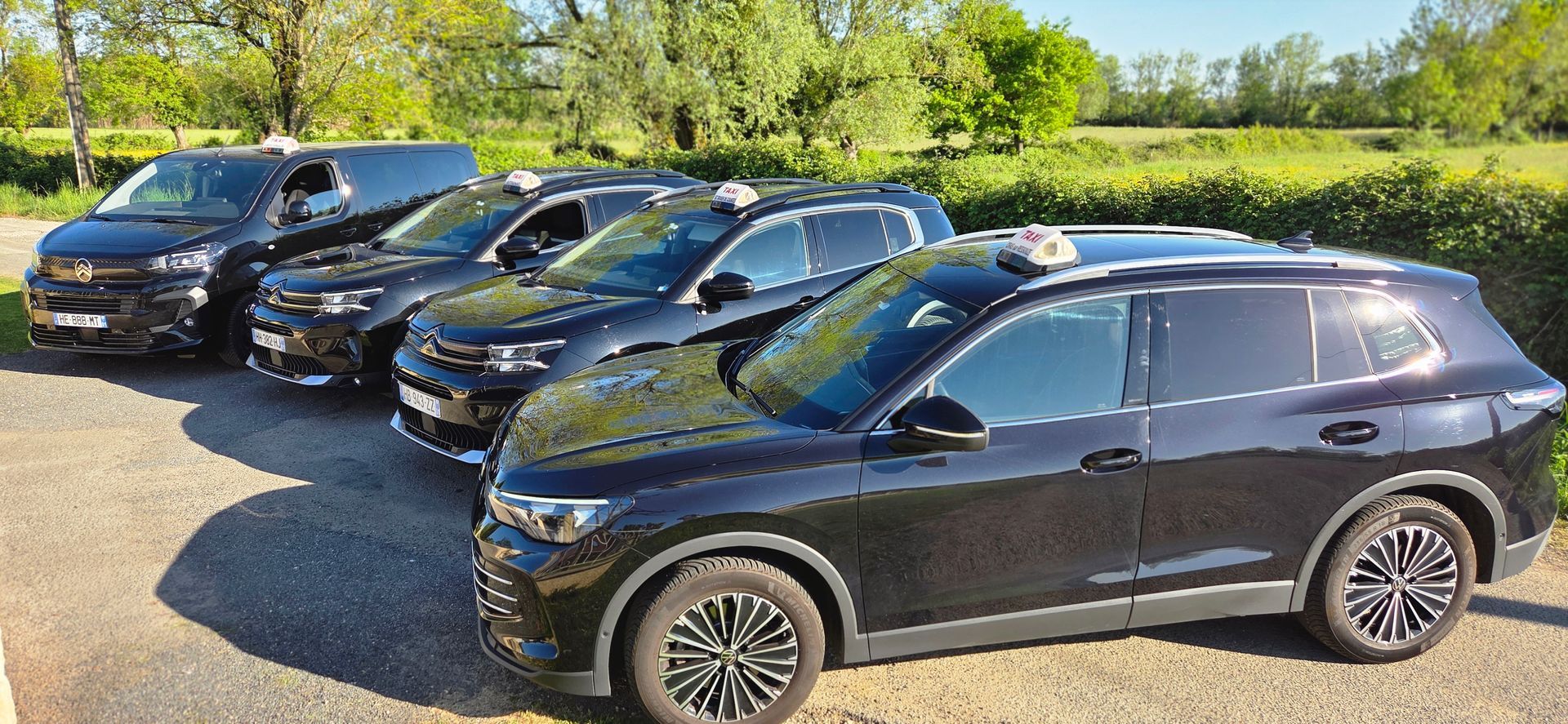 Trois SUV et un minibus noirs garés côte à côte sur un parking en gravier