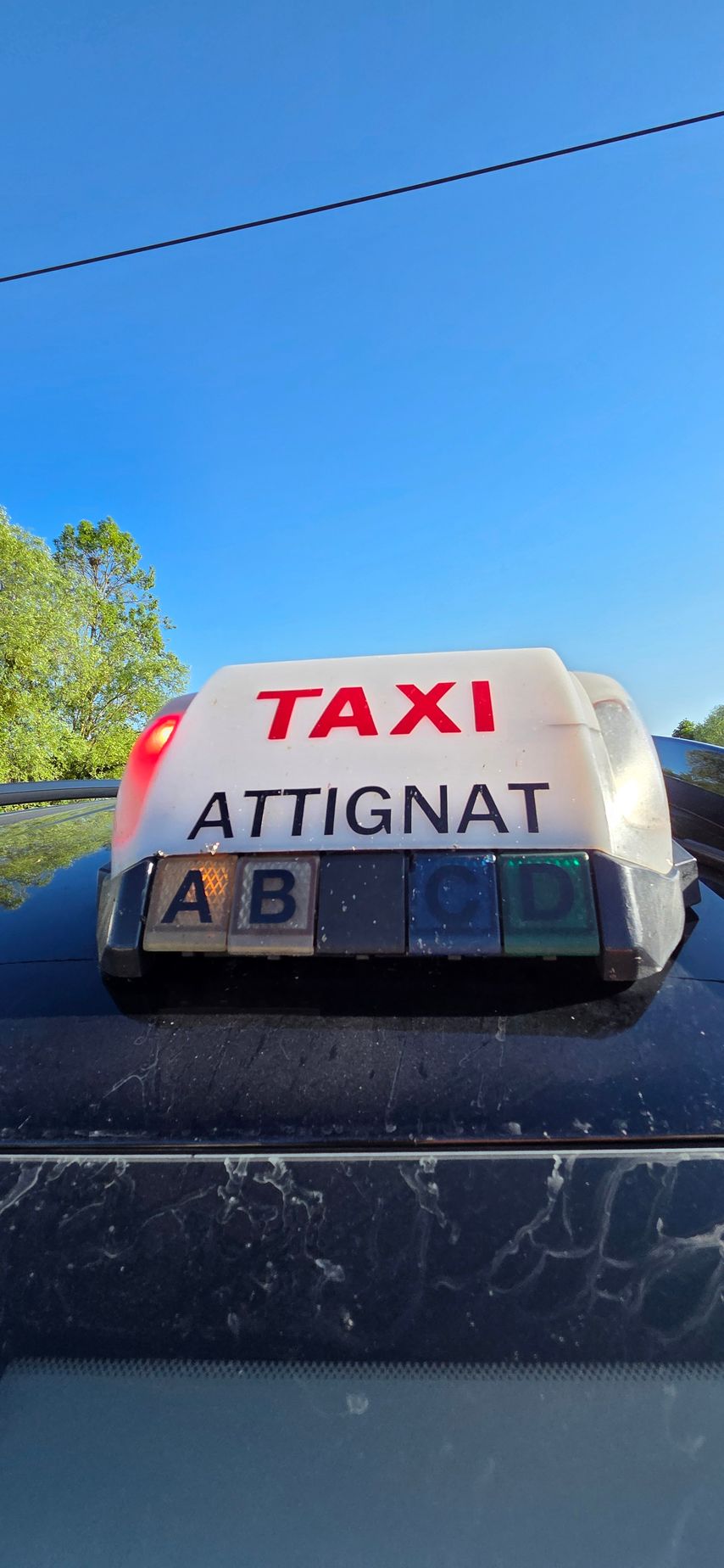 Panneau indiquant Taxi Attignat sur le toit d'un taxi, se détachant sur un ciel bleu.