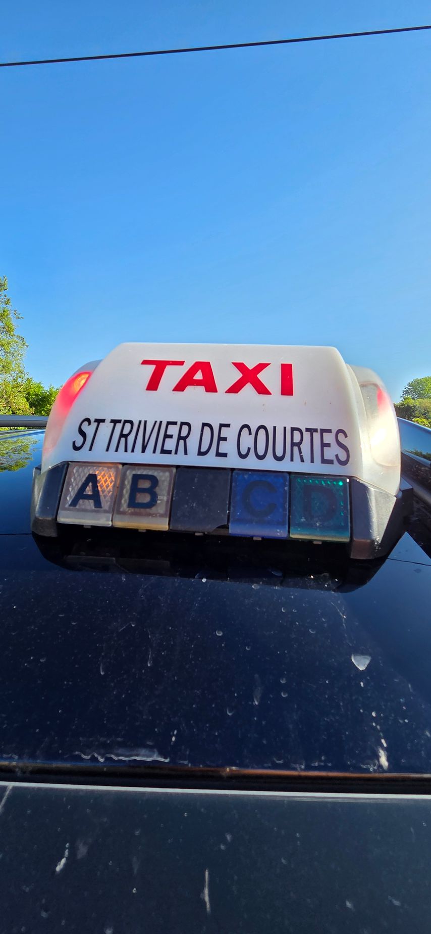 Panneau sur le toit d'un taxi indiquant Taxi en lettres rouges et Saint-Trivier-de-Courtes en lettres noires.