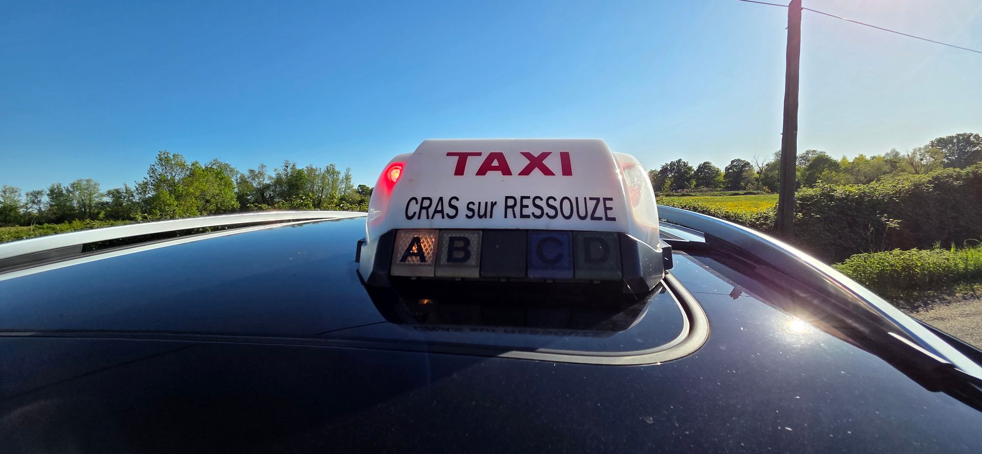 Panneau sur le toit d'un taxi indiquant Taxi en lettres rouges et Attignat en lettres noires.
