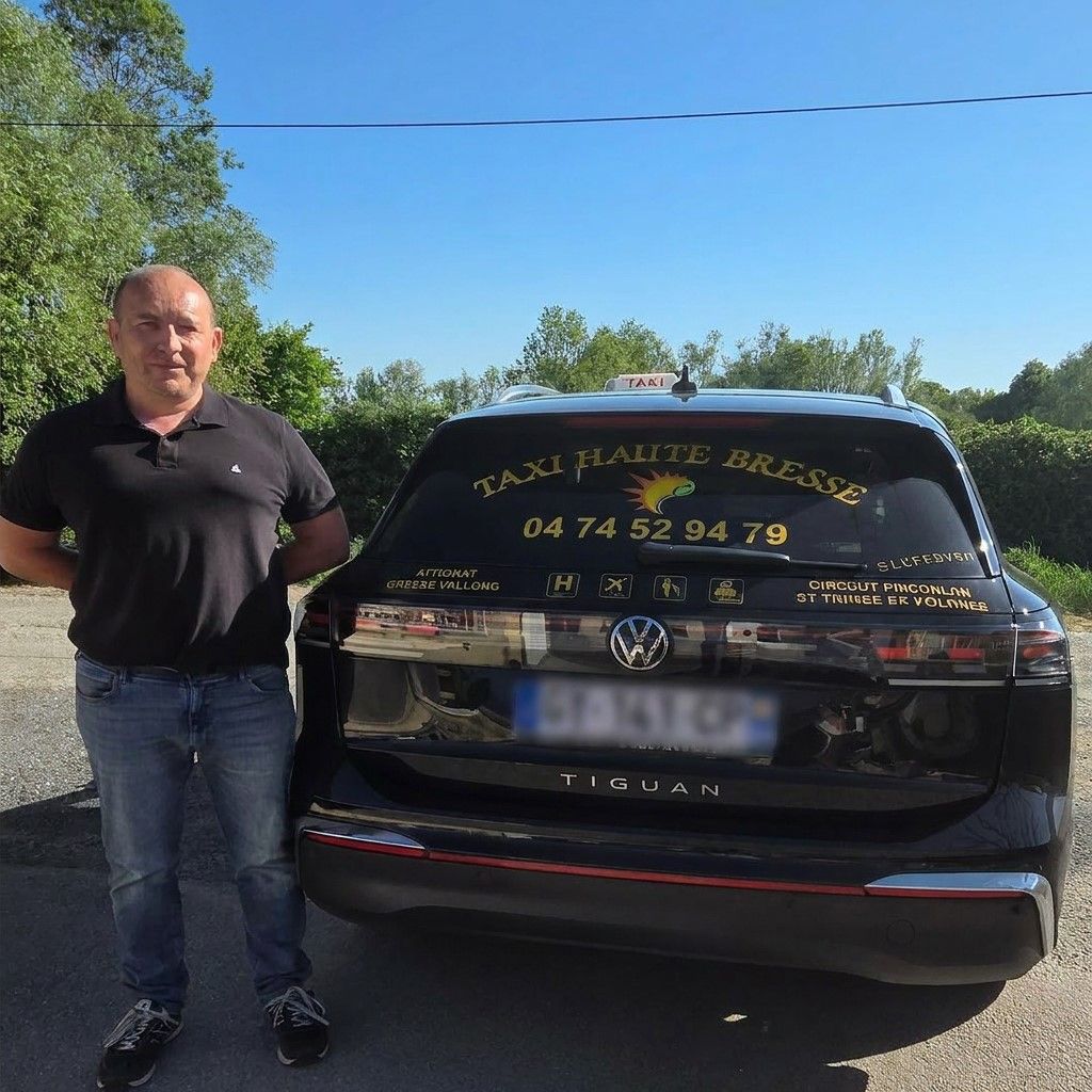 Un homme souriant se tient debout à côté d'une voiture noire sur une route ensoleillée.