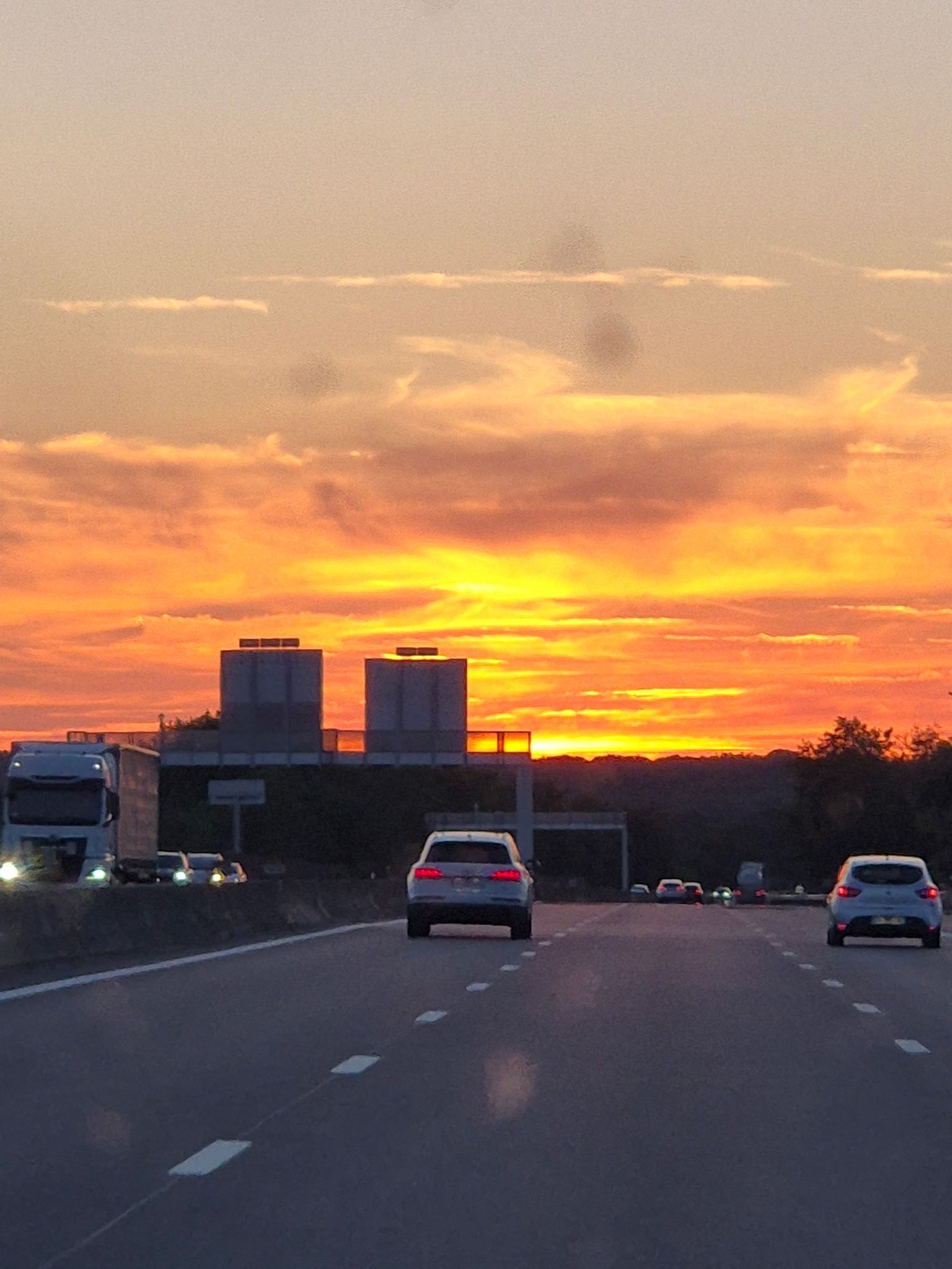 Voitures sur une autoroute au coucher du soleil, avec un ciel orange vif et des immeubles de ville au loin.