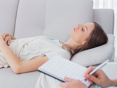 Una mujer está acostada en un sofá mientras una persona escribe en un cuaderno.