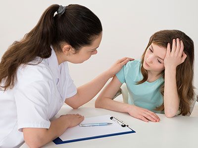 Una enfermera está consolando a una niña que está sentada en una mesa.